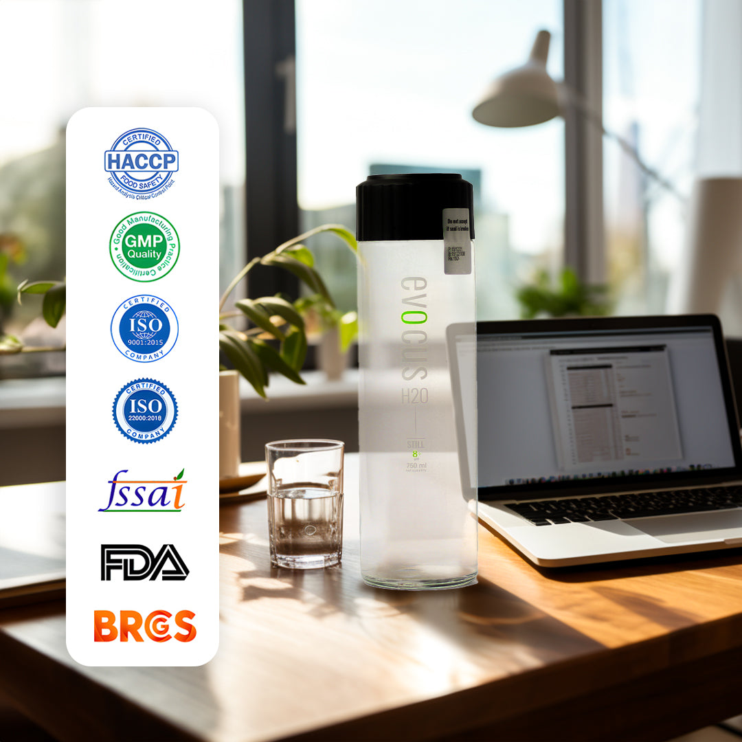 A Glass bottle of Evocus Still Alkaline Water sits on a desk beside a laptop. Text highlights certifications like HACCP, GMP, ISO 9001, ISO 22000, FSSAI, FDA, and BRCGS.