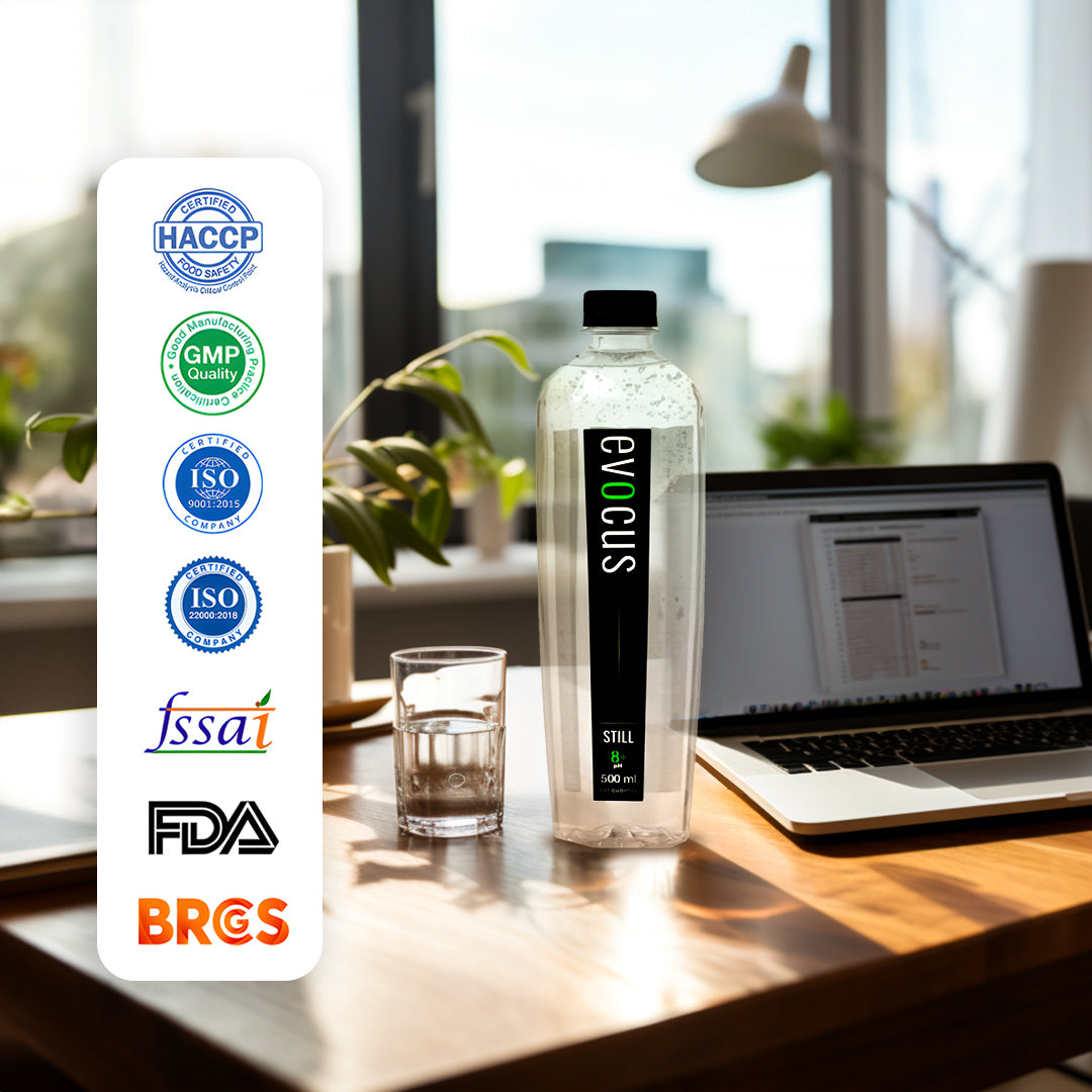 A clear bottle of Evocus Still Alkaline Water sits on a desk beside a laptop. Text highlights certifications like HACCP, GMP, ISO 9001, ISO 22000, FSSAI, FDA, and BRCGS.