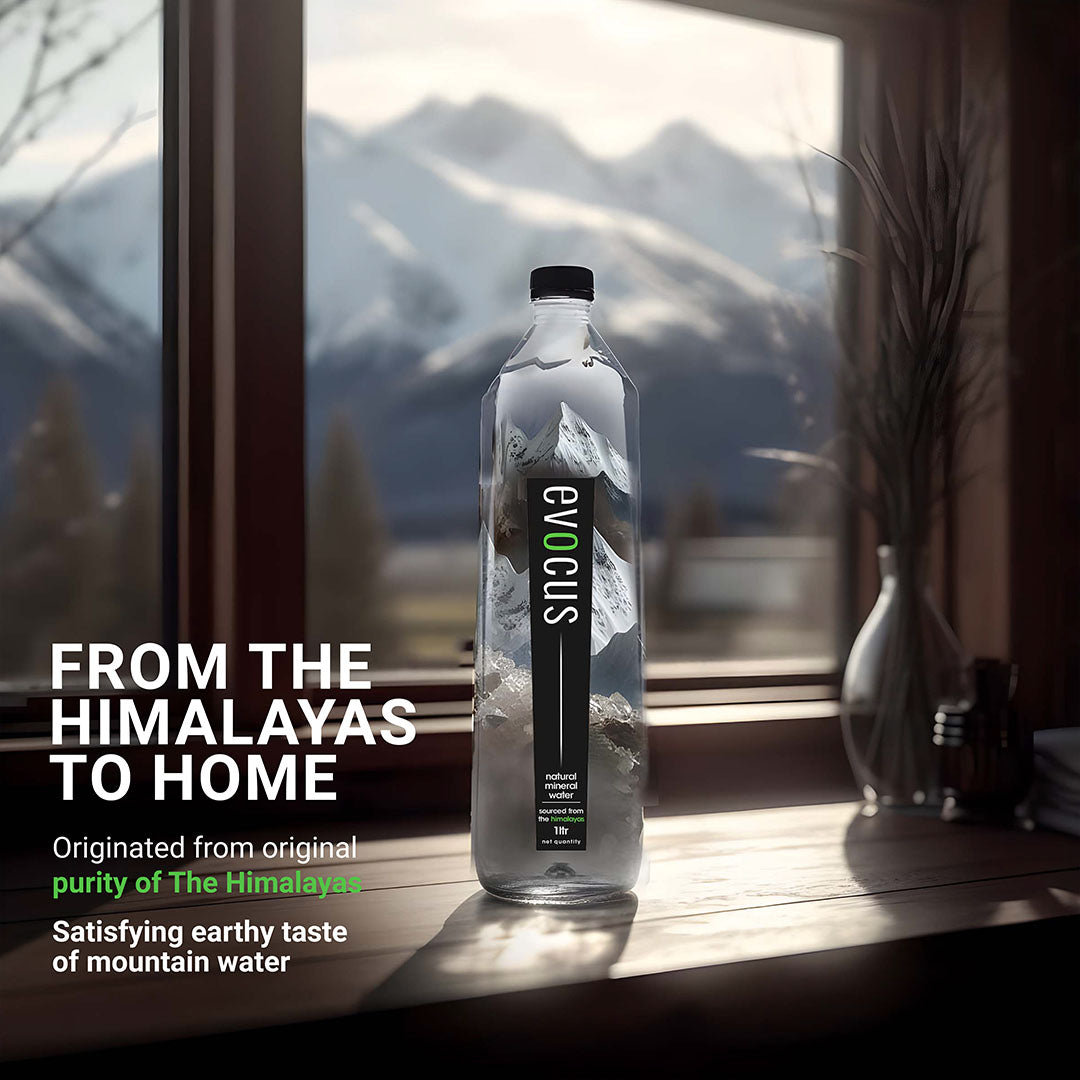 A clear bottle of Evocus Natural Mineral Water sits on a wooden table near a window. Text emphasizes its origin from the Himalayas.